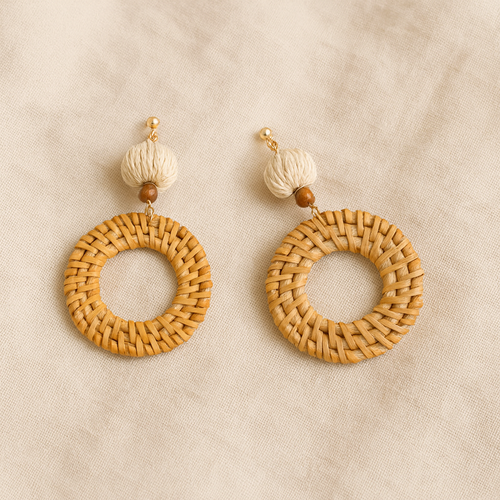 Pair of round hand-woven rattan earrings with natural fiber beads on beige fabric background.