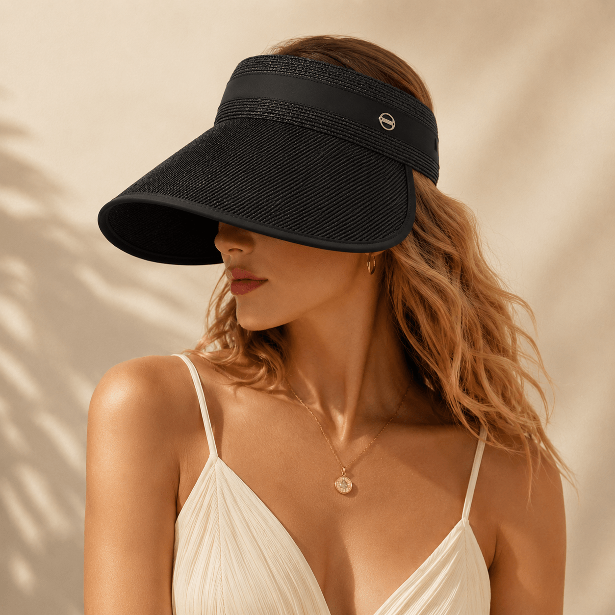 Blonde model wearing a black wide brim straw visor in soft sunlight for a modern summer look.