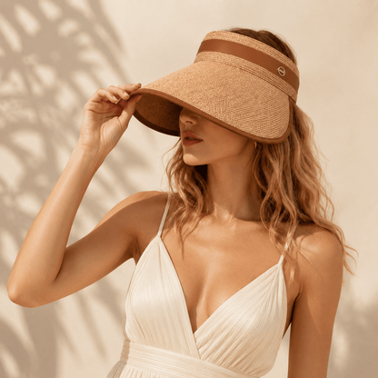 Blonde model wearing a khaki wide brim straw sun visor with a lightweight white dress in soft natural light.