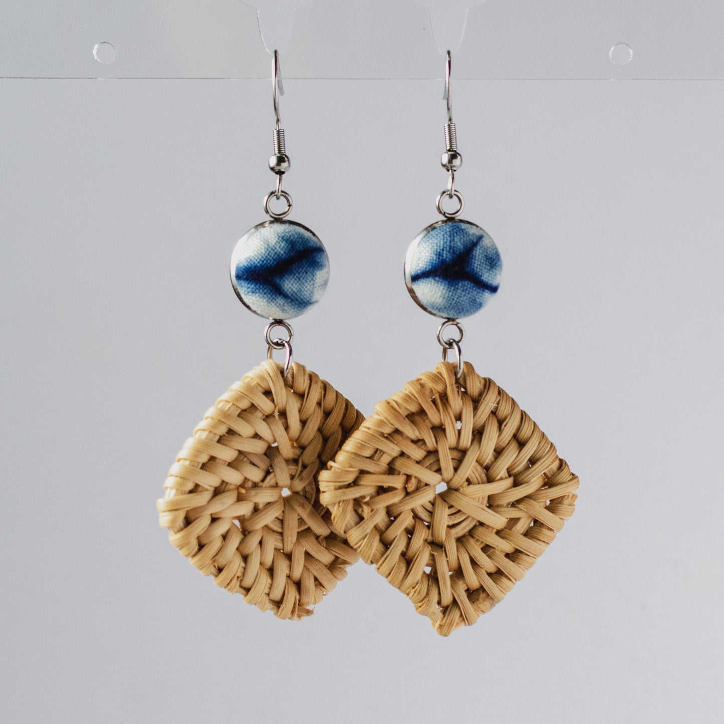 Pair of handmade square woven straw earrings with blue ceramic beads hanging on hooks.
