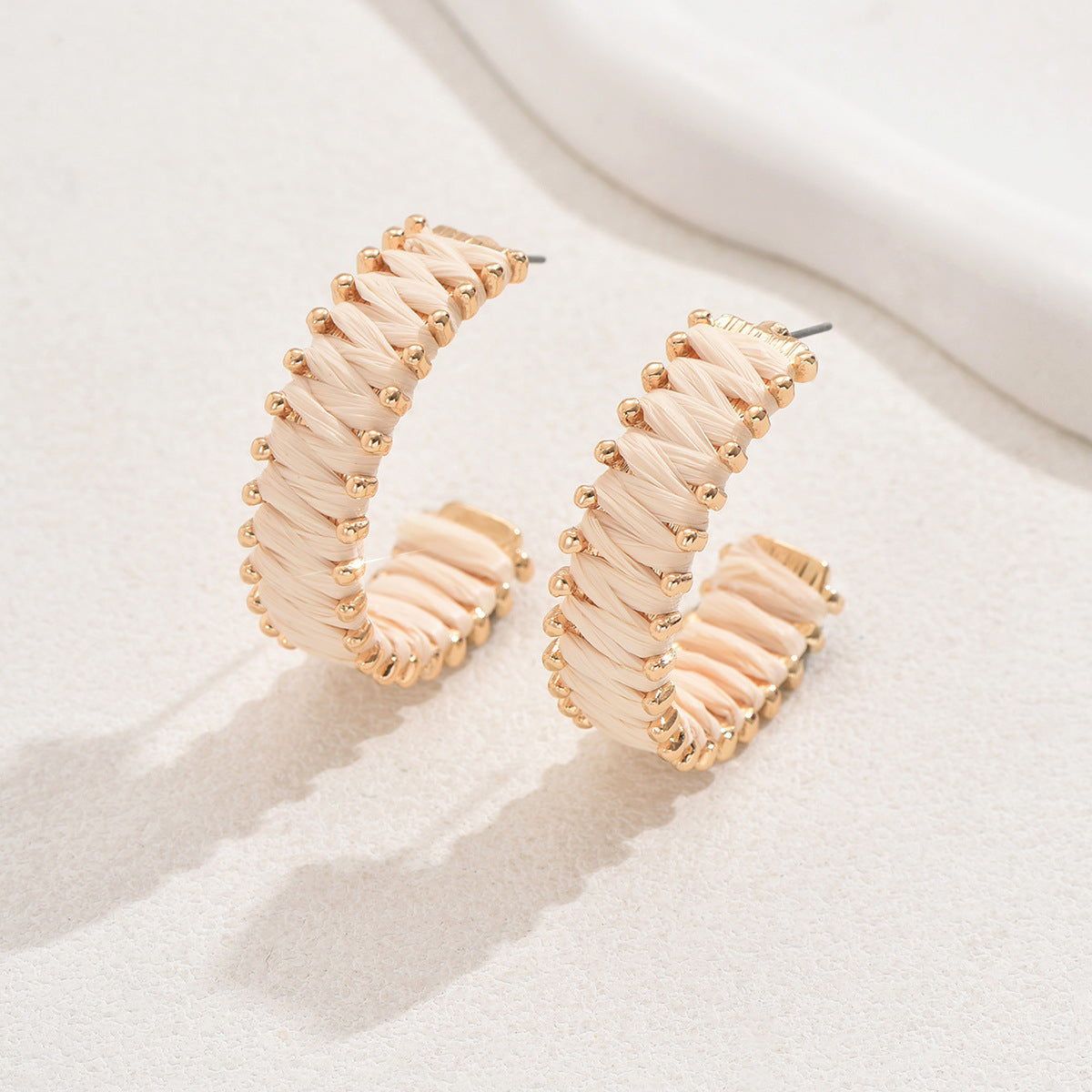Handwoven straw hoop earrings with gold details displayed on white textured background.