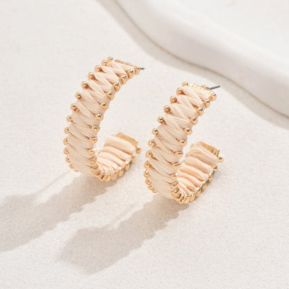 Handwoven straw hoop earrings with gold details displayed on white textured background.