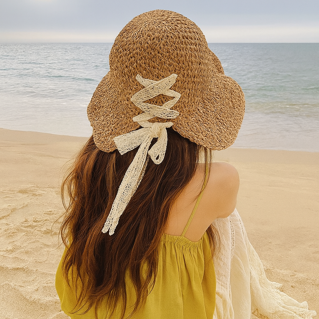 Woman wearing lace ribbon straw hat on the beach, photographed from behind with ocean view.