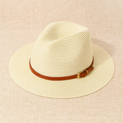 Beige woven straw Panama hat with brown belt accent, shown on textured linen surface.