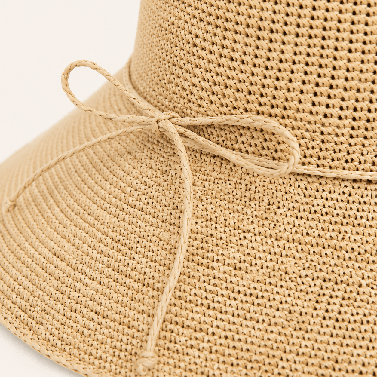 Detail view of beige wide brim straw hat with natural woven texture and side bow
