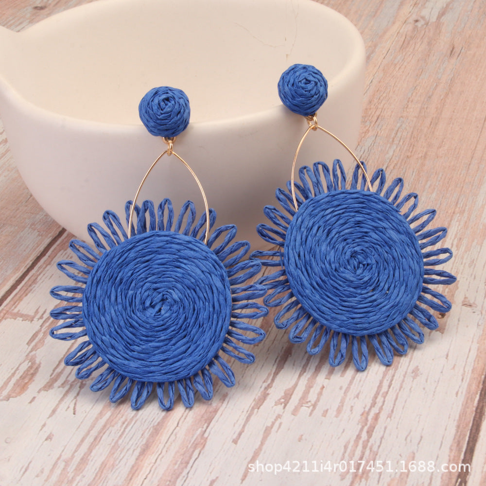 Blue woven sunflower earrings made of natural Lafite grass with gold hooks on wood surface.