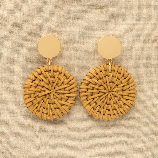 Handcrafted round rattan earrings with golden stud tops, displayed on beige linen background in natural light.