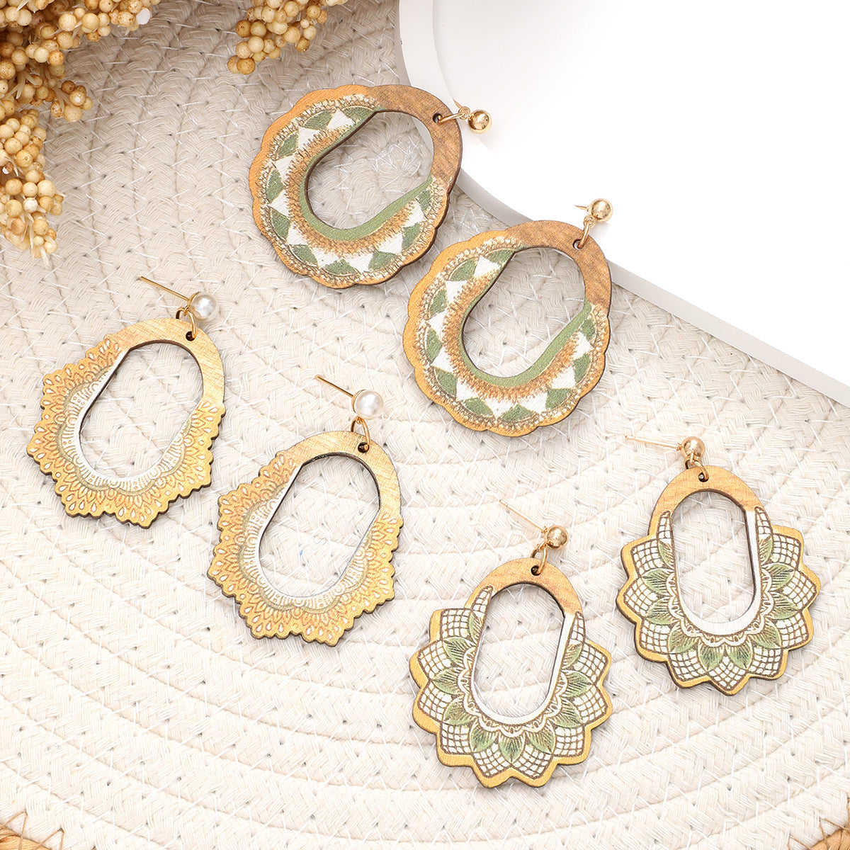 Set of assorted wooden earrings in green and white boho designs laid out on round woven mat.