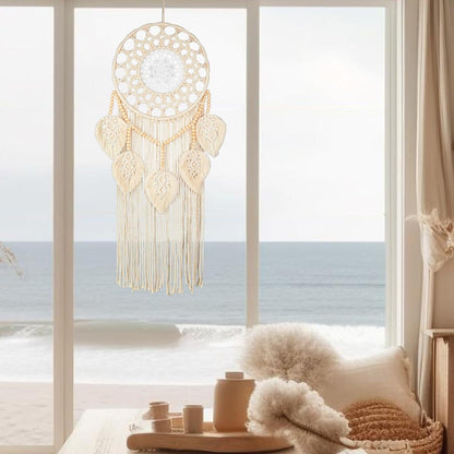 Handwoven macrame leaf tapestry hanging by a window overlooking the ocean in a serene coastal interior.