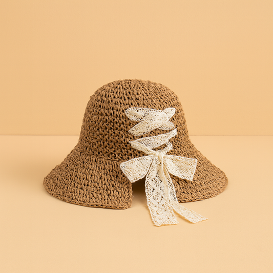 Brown woven straw hat with cream lace ribbon bow, displayed on beige background in natural lighting.