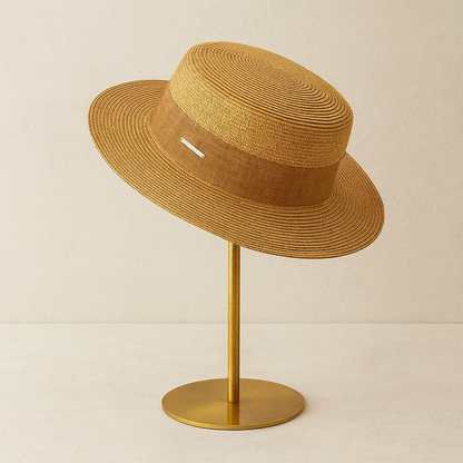 Camel-toned straw hat with linen band displayed on gold base stand, showing refined craftsmanship.