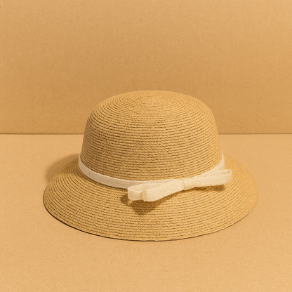 Classic woven straw hat with cream bow detail, displayed on warm beige background for a minimalist summer look.