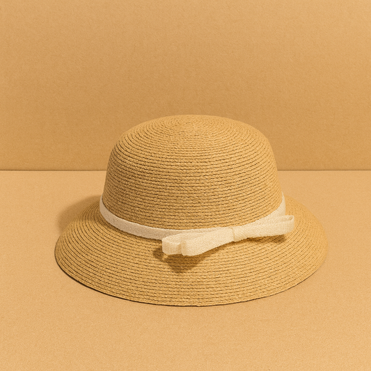 Classic woven straw hat with cream bow detail, displayed on warm beige background for a minimalist summer look.