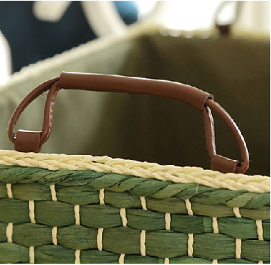 Close-up of brown leather handle attached to the handwoven green straw storage basket.