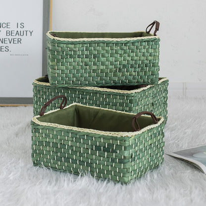 Set of three stackable green woven storage baskets with leather handles arranged vertically on a soft white rug.