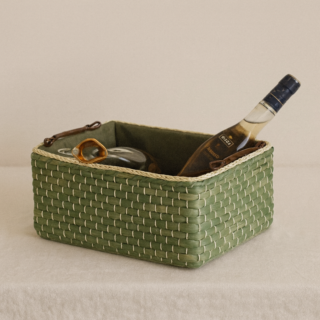 Green straw storage basket used for kitchen or pantry organization, holding bottles and utensils.