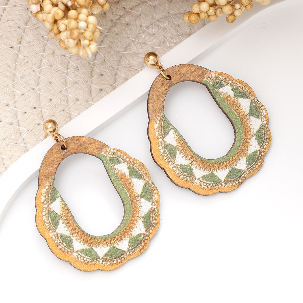 Pair of wooden oval earrings with green and white embroidery displayed on white background.