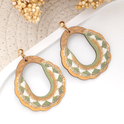 Pair of wooden oval earrings with green and white embroidery displayed on white background.