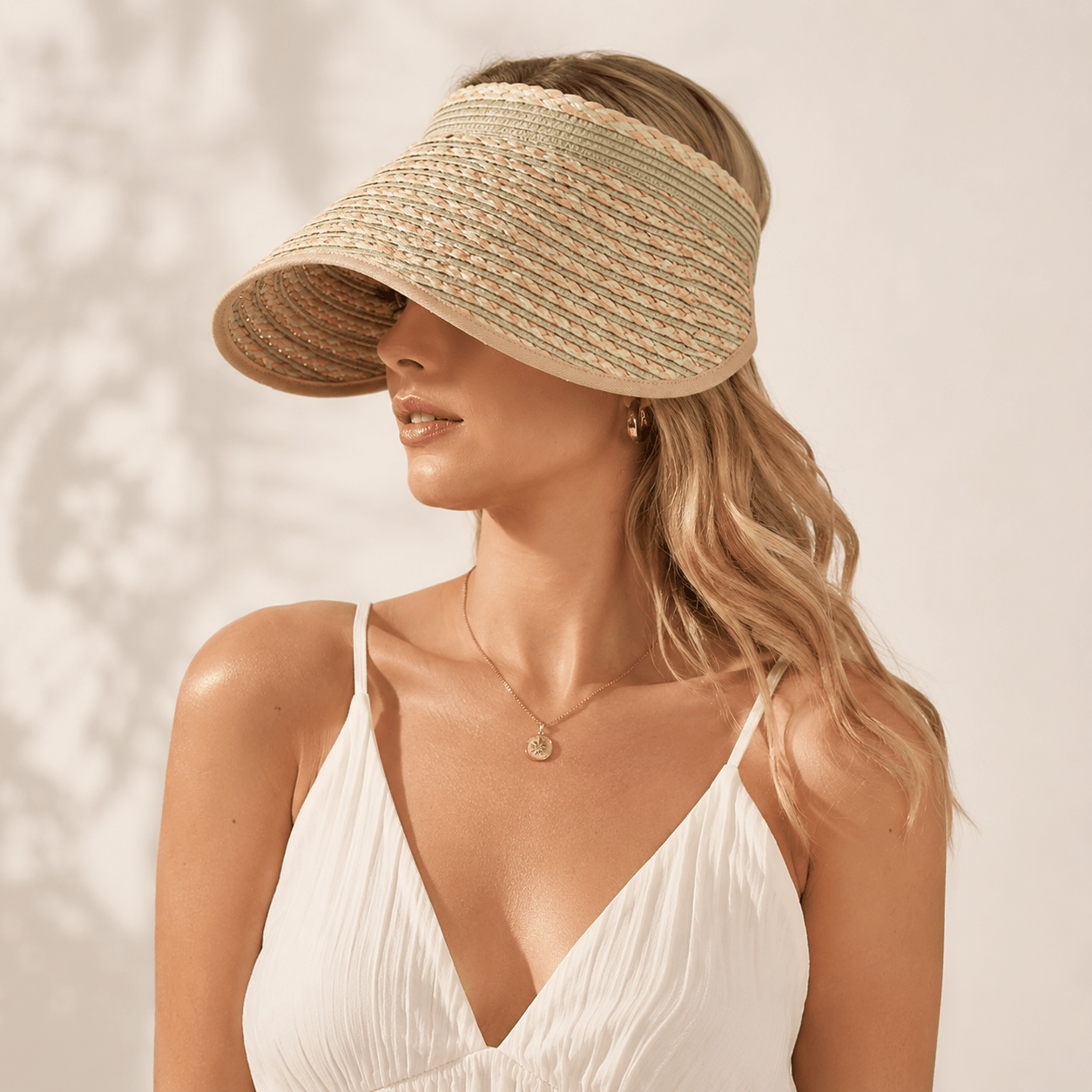 Side portrait of a woman wearing a green khaki wide brim straw sun visor with a white dress