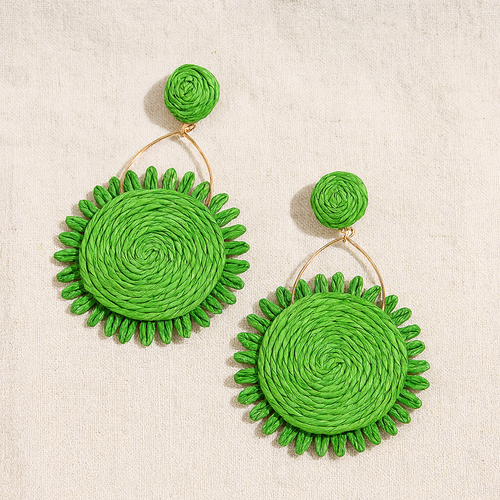 Green natural Lafite grass sunflower earrings with spiral woven pattern on beige linen background.
