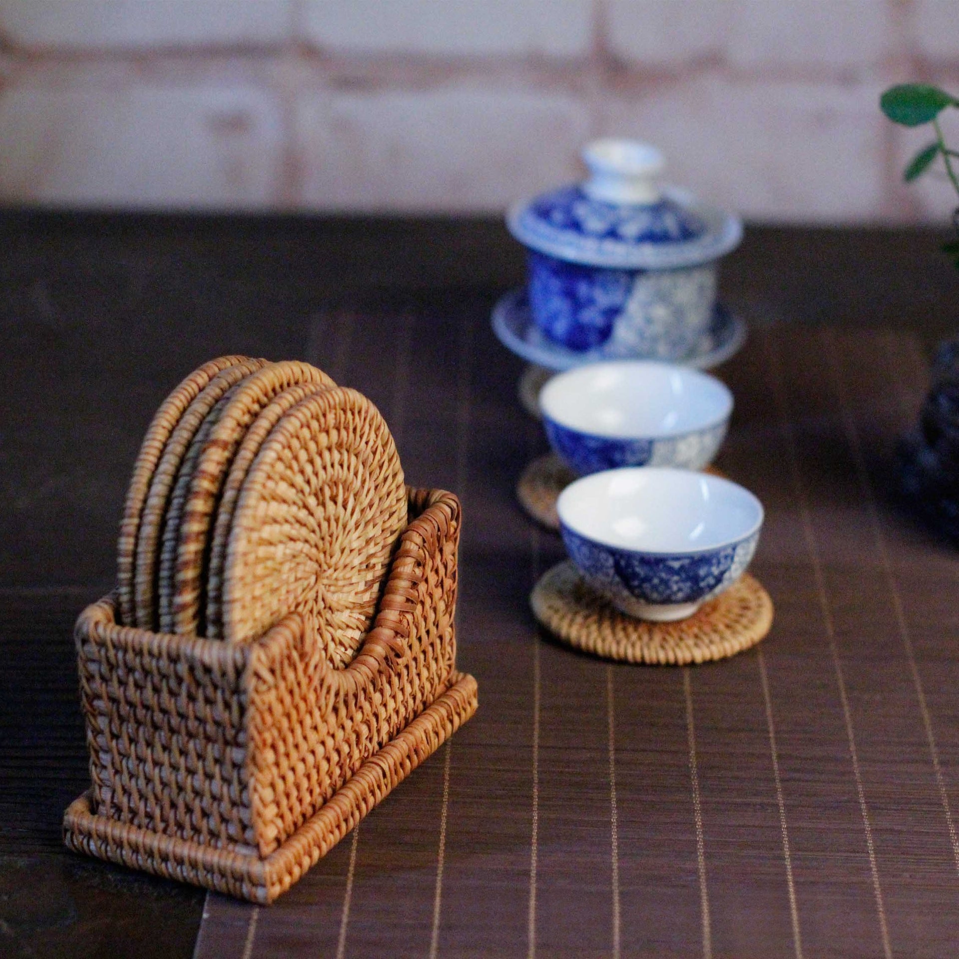 Rattan coaster set placed beside traditional Chinese tea cups with dark wood background.