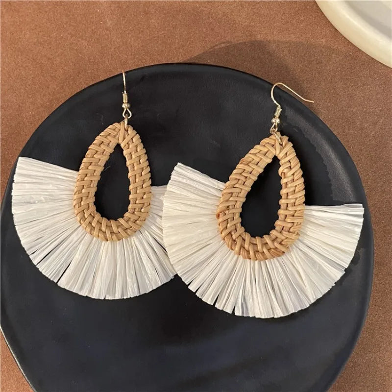 Handmade rattan earrings with white raffia fan design placed on dark plate background.