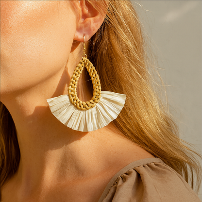 Close-up of handmade rattan teardrop earring with white raffia fan worn by woman in natural sunlight.