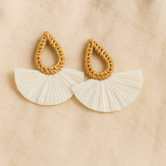 Pair of handmade rattan teardrop earrings with white raffia fan design on beige fabric background.