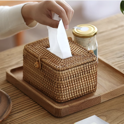Hand pulling tissue from handmade rattan tissue box on wooden tray beside coffee and breakfast items.