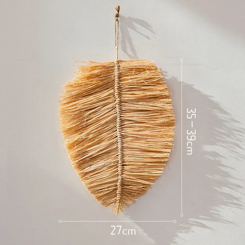 Leaf-shaped raffia straw wall hanging with hand-woven spine detail, measuring 35–39 cm in height.
