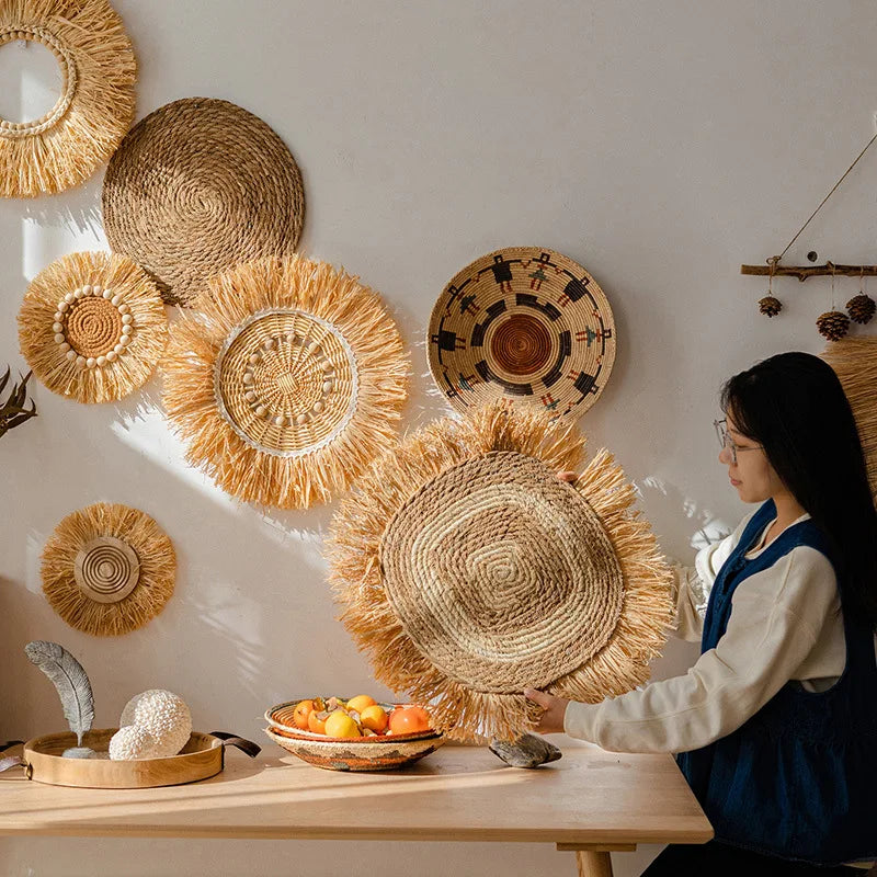 Woman arranging round raffia straw wall hangings in a sunlit home interior with natural and bohemian decor.