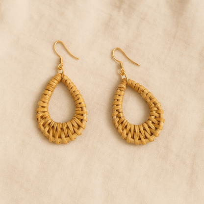 Pair of handwoven rattan teardrop dangle earrings with gold hooks on beige linen background.
