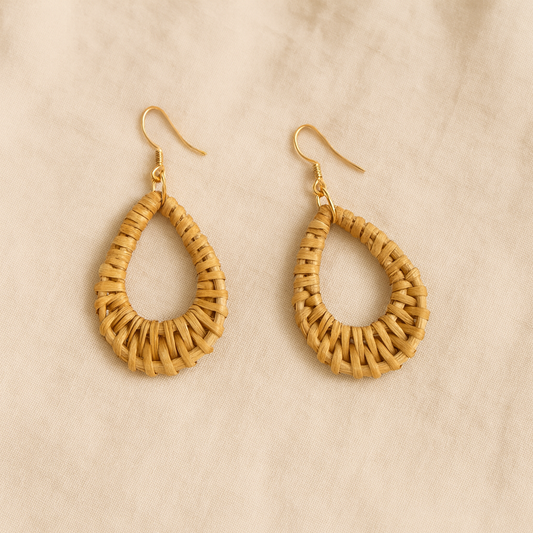 Pair of handwoven rattan teardrop dangle earrings with gold hooks on beige linen background.