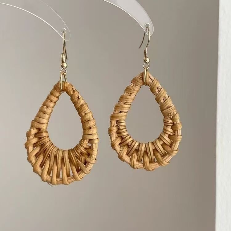 Pair of natural rattan teardrop earrings hanging on transparent acrylic holder.
