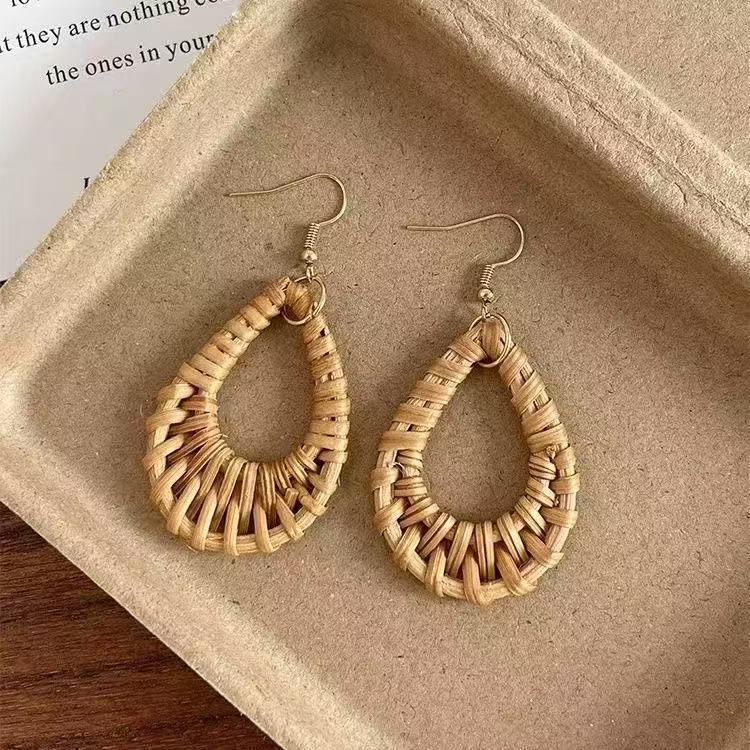 Handwoven rattan dangle earrings placed on recycled kraft paper tray with natural texture.
