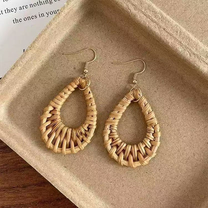 Handwoven rattan dangle earrings placed on recycled kraft paper tray with natural texture.