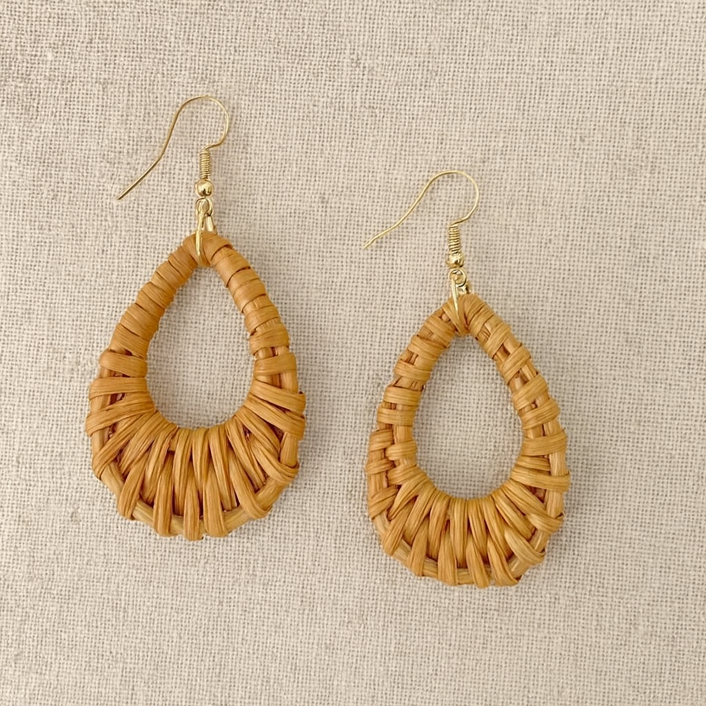 Handwoven rattan teardrop earrings with gold hooks displayed on neutral linen fabric.