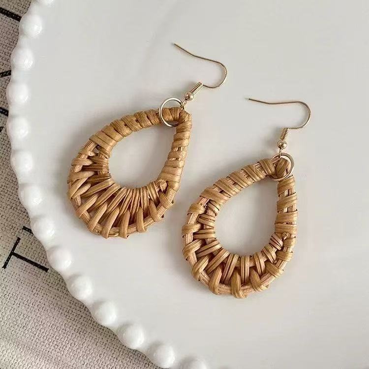 Pair of rattan teardrop earrings with gold hooks displayed on white ceramic plate.