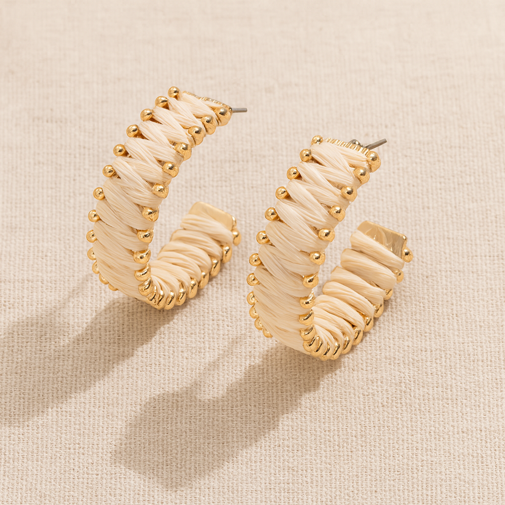 Handwoven straw hoop earrings with gold accents on beige linen background.