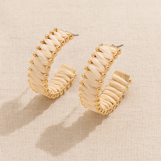 Handwoven straw hoop earrings with gold accents on beige linen background.