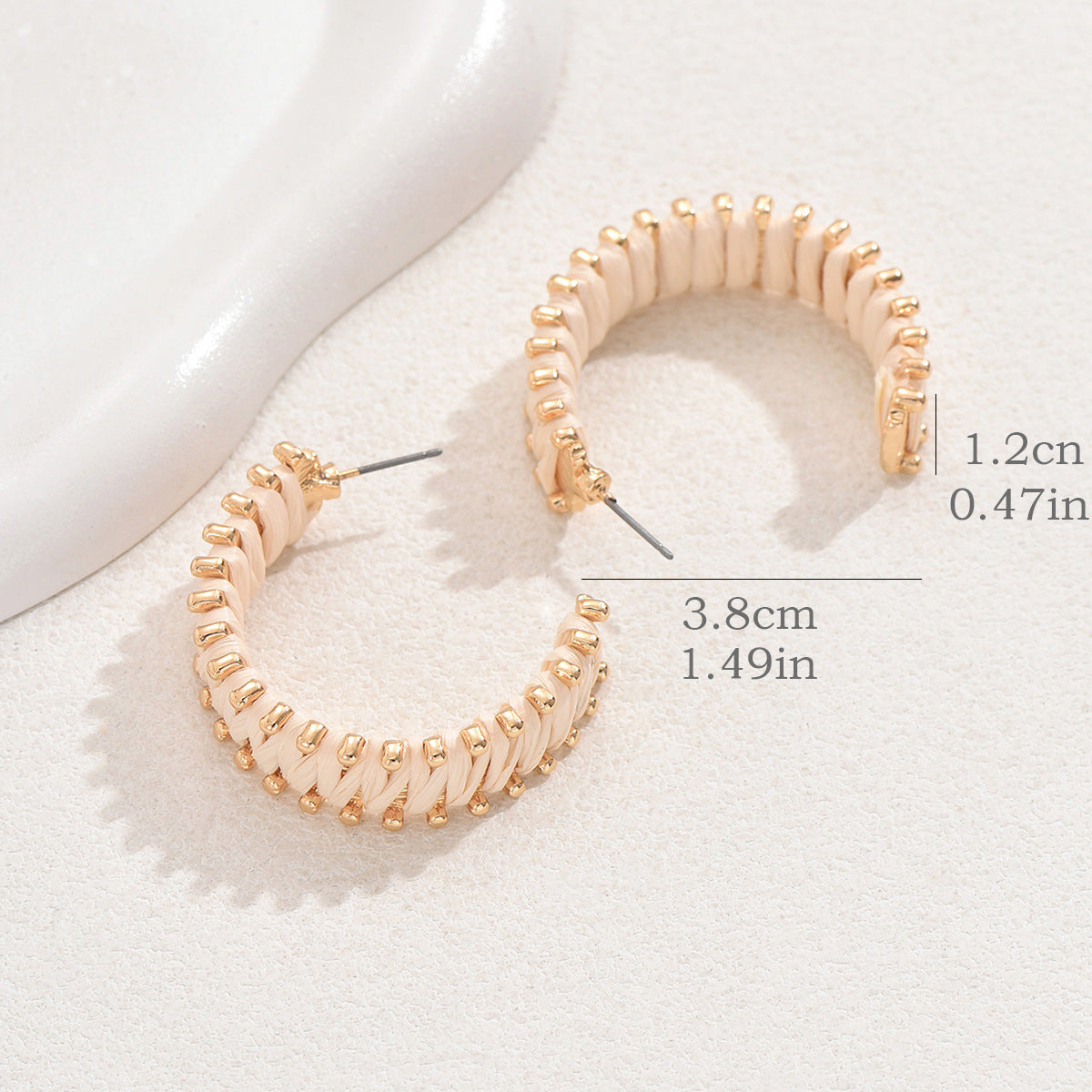 Size reference of handwoven straw hoop earrings with gold details on light surface.