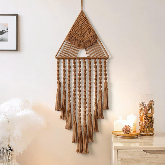 Handwoven brown macrame wall hanging with triangular top and tassel strands, displayed beside candles.