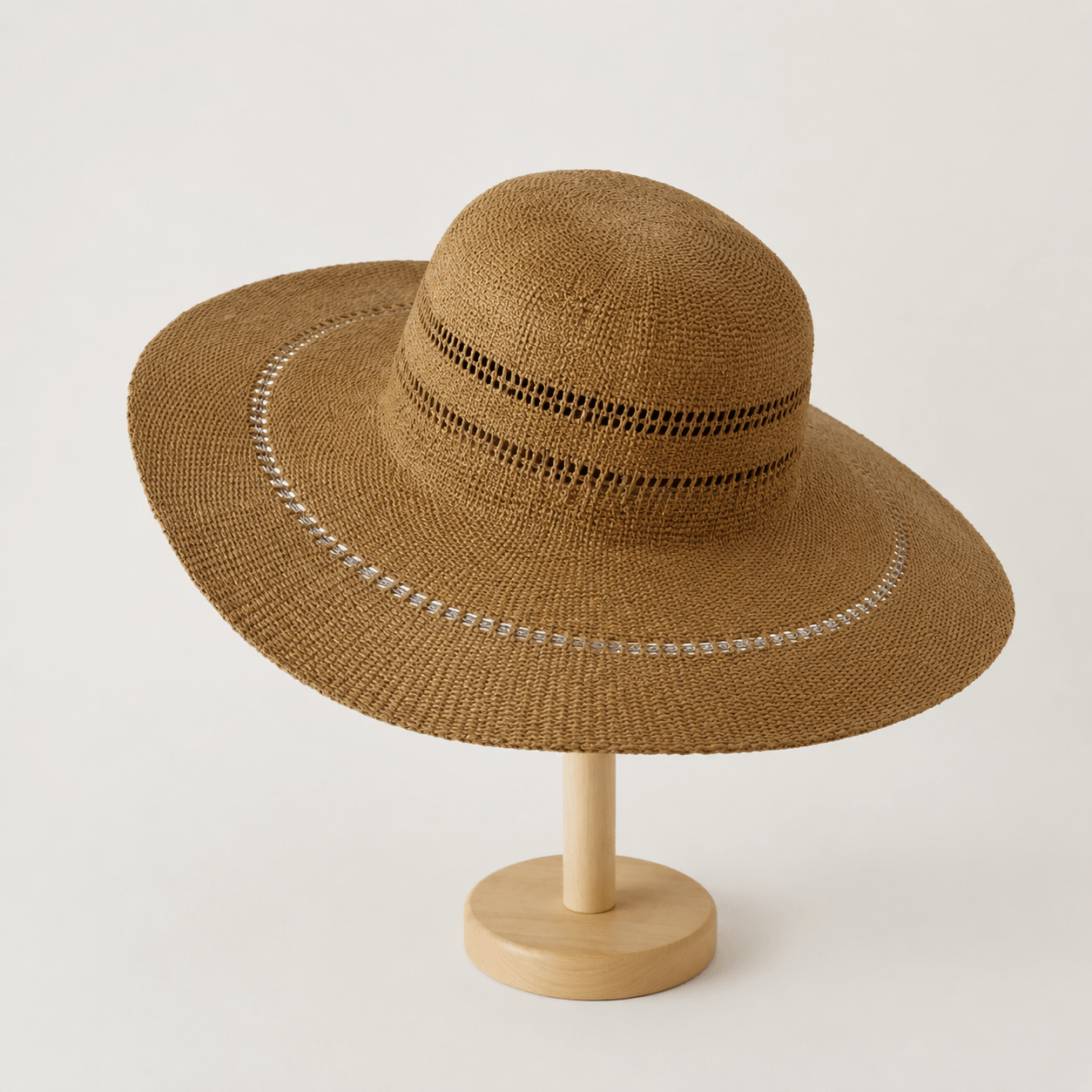 Khaki handwoven wide brim paper straw hat displayed on a wooden stand with openwork crown detail