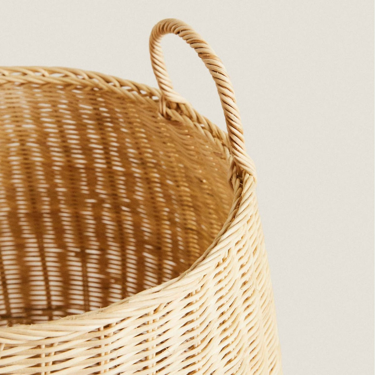 Close-up of basket rim and interior weave showing sturdy loop handle and tight rattan pattern.