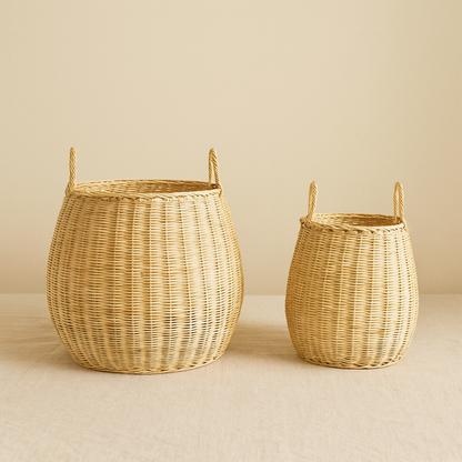 Pair of natural rattan laundry baskets on neutral backdrop, rounded bucket shape with double handles.