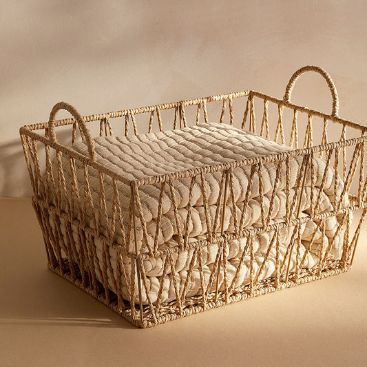 Large handwoven rattan storage basket with quilt inside and two loop handles, warm studio lighting.