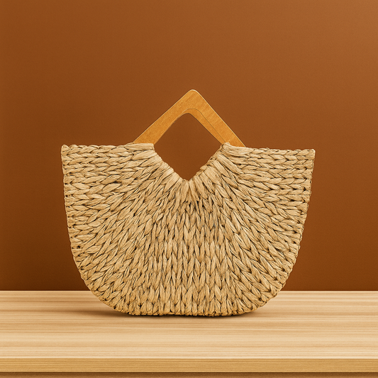 A large handwoven straw tote bag with a fan-shaped silhouette and geometric wooden handles, placed on a wooden surface against a warm brown background.