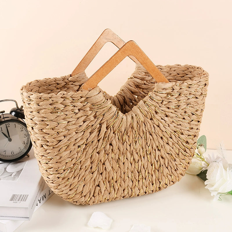 Handwoven straw tote bag with wooden handles placed beside white flowers and books, showing elegant natural texture.