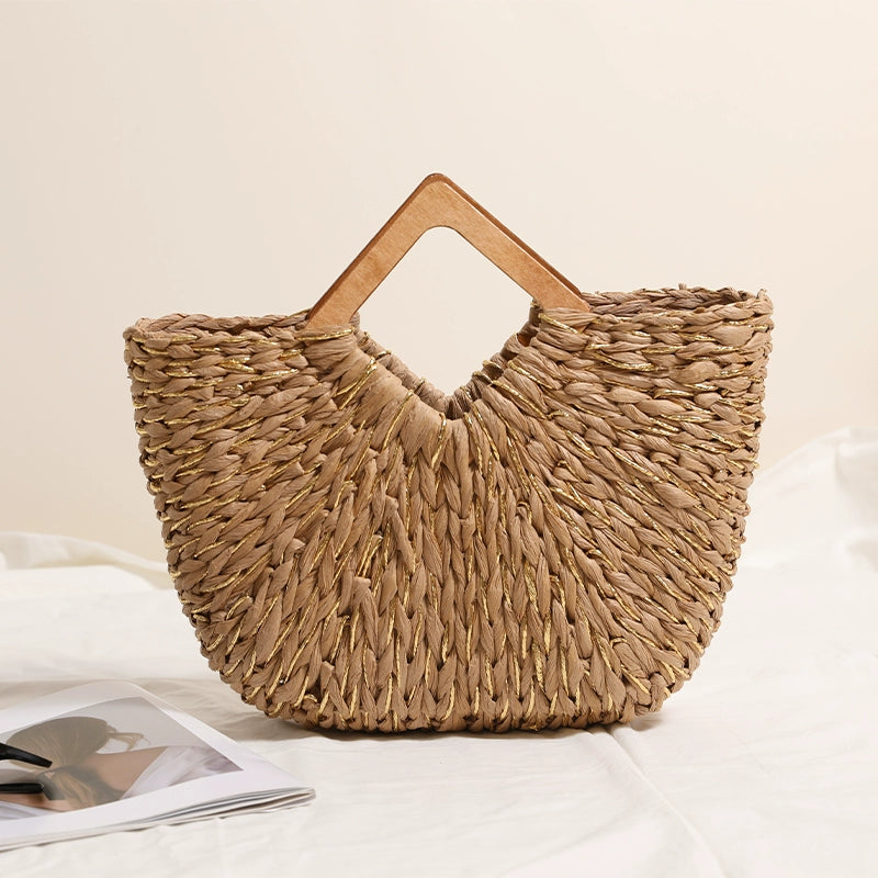 Handwoven straw tote bag with wooden handles placed on a white cloth surface next to an open magazine.