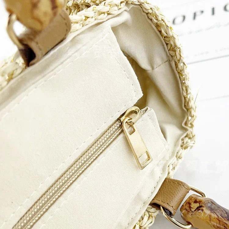 Close-up of the inner zipper pocket of the straw tote bag, featuring cream fabric lining and gold-tone zipper pull.